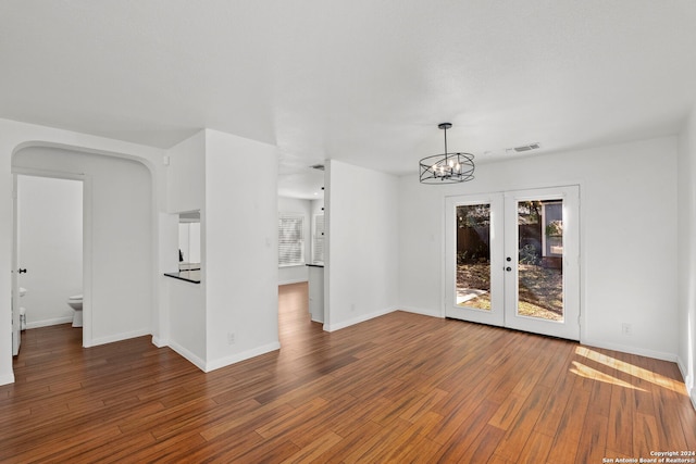 empty room with dark hardwood / wood-style floors, an inviting chandelier, and french doors