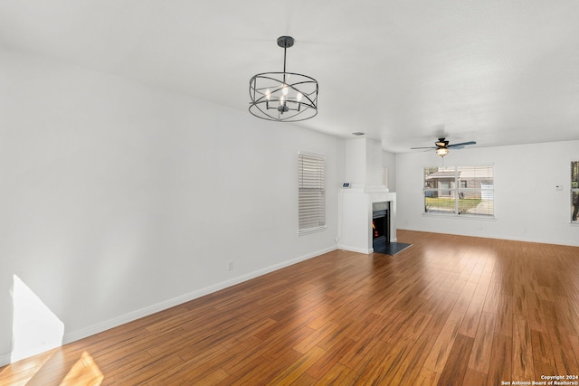 unfurnished living room with a fireplace, ceiling fan with notable chandelier, and hardwood / wood-style flooring