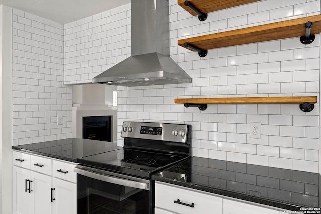 kitchen with electric range, wall chimney exhaust hood, white cabinets, and dark stone counters