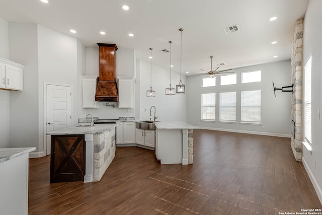 kitchen with ceiling fan, white cabinets, custom range hood, sink, and hanging light fixtures