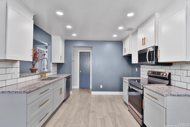 kitchen with light hardwood / wood-style floors, sink, light stone counters, appliances with stainless steel finishes, and white cabinetry