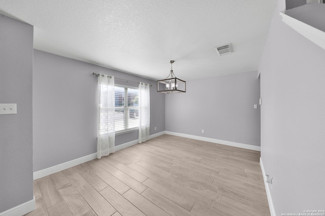 unfurnished dining area with a textured ceiling, a chandelier, and light hardwood / wood-style flooring