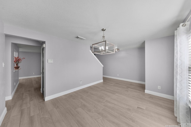 unfurnished living room featuring a notable chandelier and light hardwood / wood-style flooring