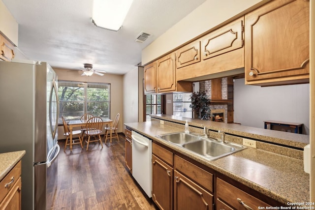 kitchen featuring a fireplace, stainless steel refrigerator, sink, dark hardwood / wood-style flooring, and white dishwasher