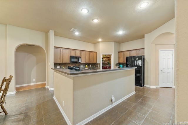 kitchen with a textured ceiling, light tile patterned floors, tasteful backsplash, and black appliances