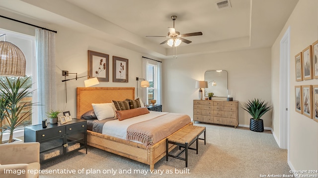 bedroom featuring a raised ceiling, light carpet, multiple windows, and ceiling fan