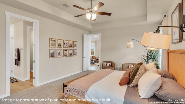 bedroom with light wood-type flooring, ceiling fan, and a tray ceiling