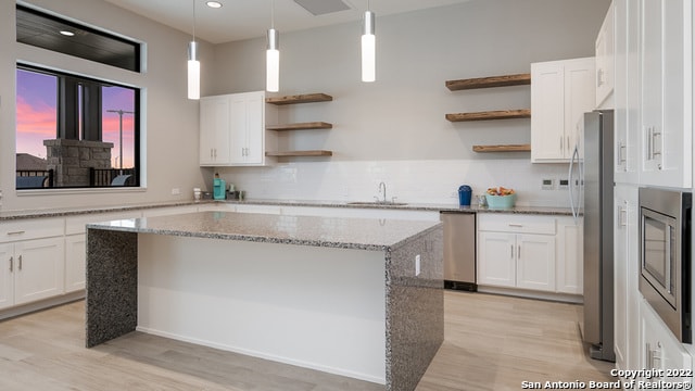 kitchen featuring light hardwood / wood-style flooring, stainless steel appliances, light stone countertops, a center island, and white cabinetry