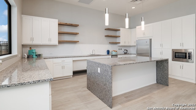 kitchen featuring light stone countertops, white cabinets, hanging light fixtures, light hardwood / wood-style flooring, and appliances with stainless steel finishes