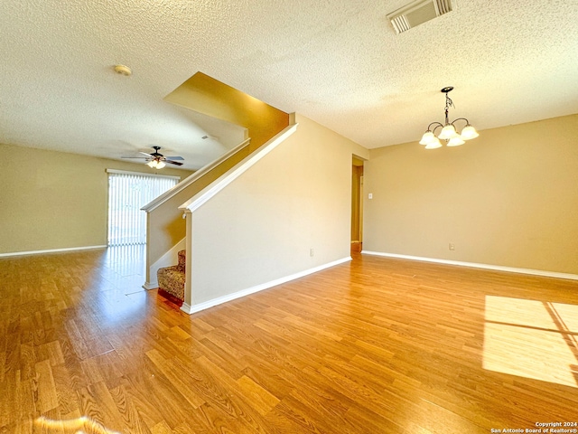 unfurnished living room with ceiling fan with notable chandelier, hardwood / wood-style flooring, and a textured ceiling