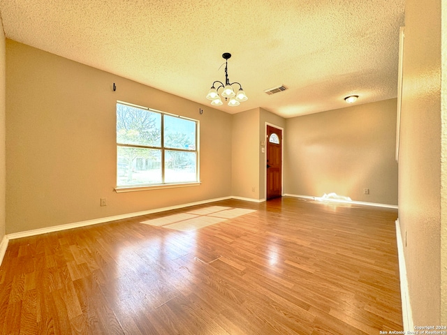 empty room with a chandelier, wood-type flooring, and a textured ceiling