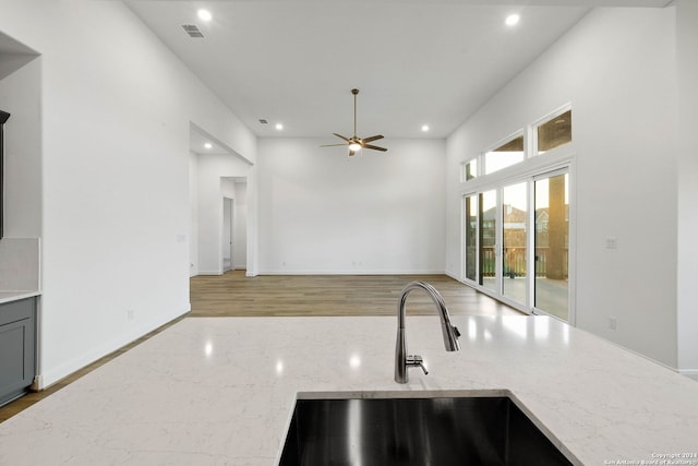 kitchen with light stone countertops, ceiling fan, sink, and light hardwood / wood-style flooring