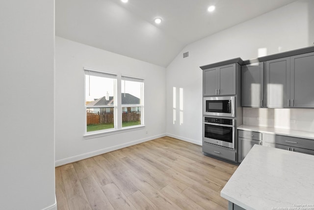 kitchen with light hardwood / wood-style floors, gray cabinets, appliances with stainless steel finishes, and vaulted ceiling