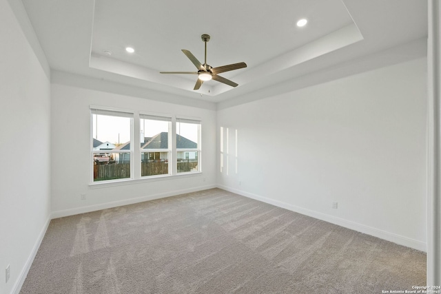 carpeted empty room featuring ceiling fan and a raised ceiling