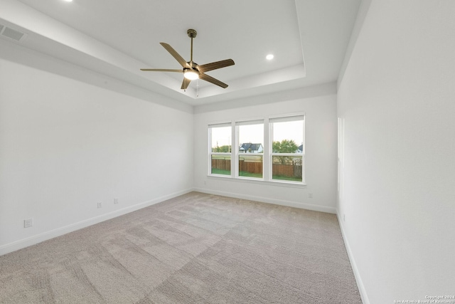 empty room featuring ceiling fan, light colored carpet, and a tray ceiling