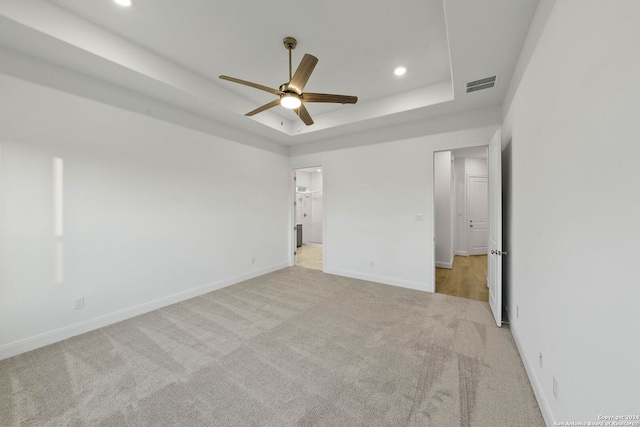 unfurnished bedroom with ceiling fan, a raised ceiling, light carpet, and a spacious closet