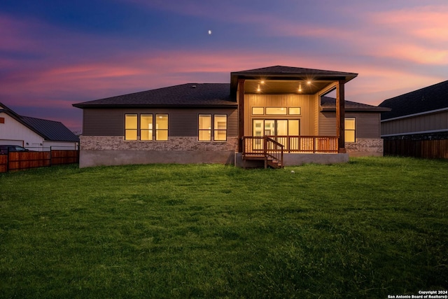 back house at dusk featuring a lawn