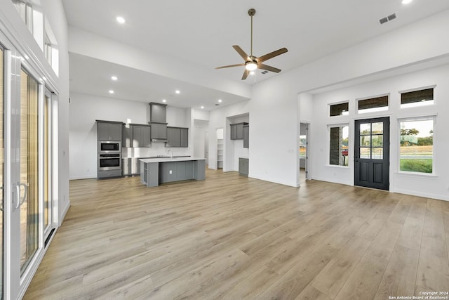 unfurnished living room featuring a towering ceiling, light hardwood / wood-style floors, sink, and ceiling fan