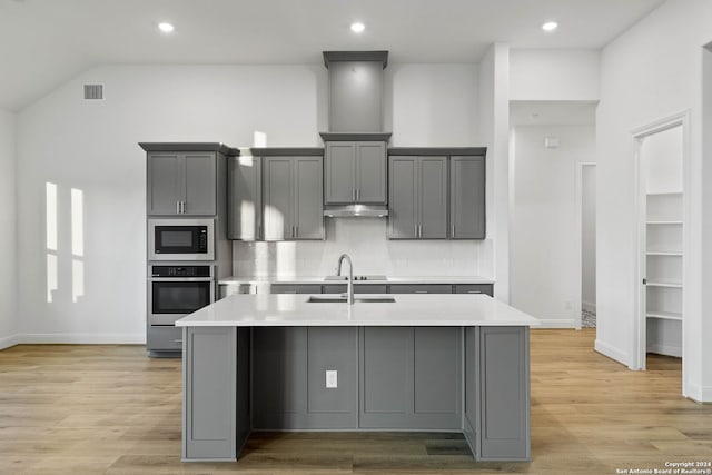 kitchen with sink, gray cabinetry, light hardwood / wood-style flooring, a center island with sink, and stainless steel appliances