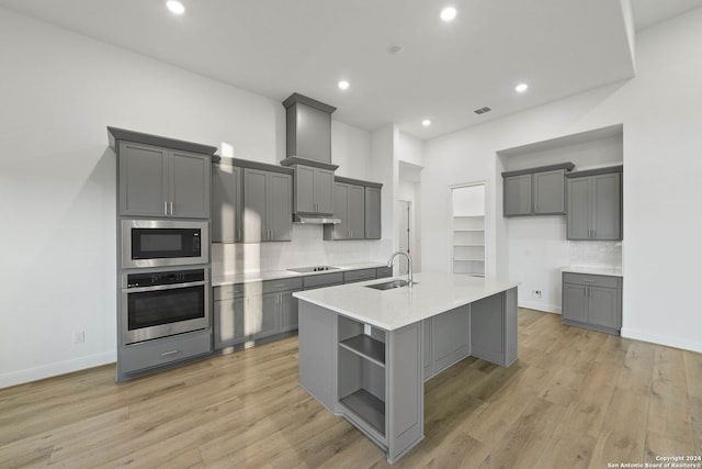 kitchen featuring gray cabinets, a kitchen island with sink, light wood-type flooring, sink, and appliances with stainless steel finishes