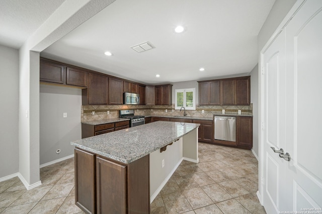 kitchen with a kitchen island, light stone countertops, decorative backsplash, sink, and appliances with stainless steel finishes