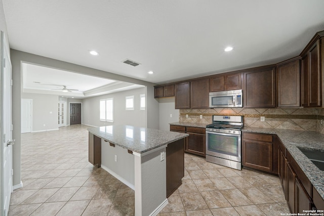 kitchen with ceiling fan, stone countertops, dark brown cabinetry, backsplash, and appliances with stainless steel finishes