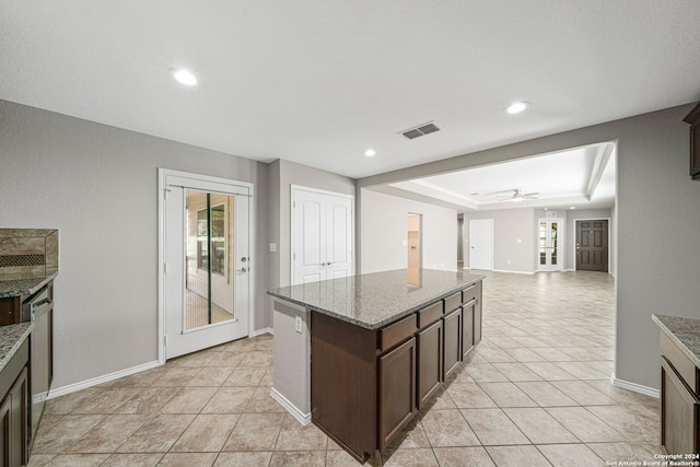 kitchen featuring a kitchen island, light stone counters, ceiling fan, a tray ceiling, and dark brown cabinets