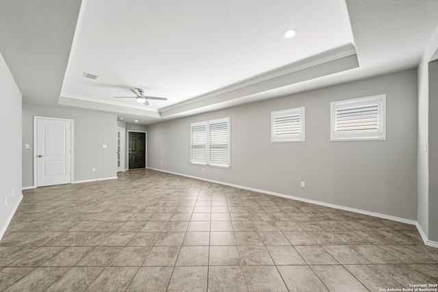 empty room with ceiling fan, a tray ceiling, and light tile patterned floors