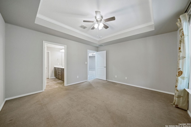 unfurnished bedroom with light carpet, ceiling fan, connected bathroom, and a raised ceiling