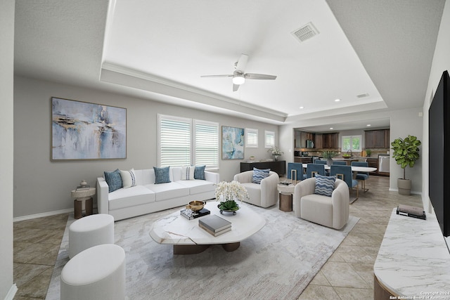 tiled living room with a tray ceiling and ceiling fan