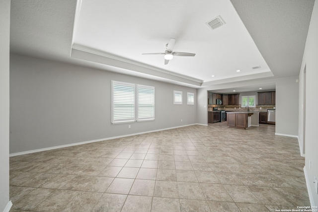 unfurnished living room featuring ceiling fan, light tile patterned flooring, a tray ceiling, and sink