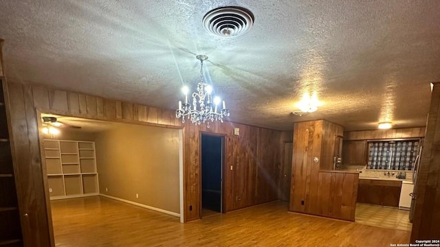 interior space featuring light hardwood / wood-style floors, an inviting chandelier, wooden walls, and a textured ceiling