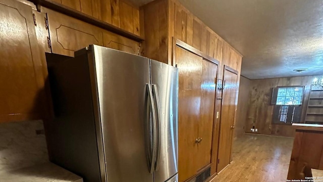 kitchen featuring stainless steel refrigerator, wood walls, and light hardwood / wood-style floors