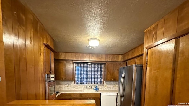 kitchen featuring stainless steel appliances, tasteful backsplash, sink, wood walls, and a textured ceiling