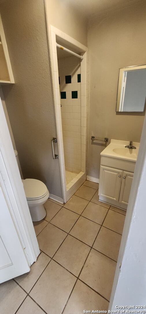 bathroom featuring tile patterned flooring, toilet, a tile shower, and vanity