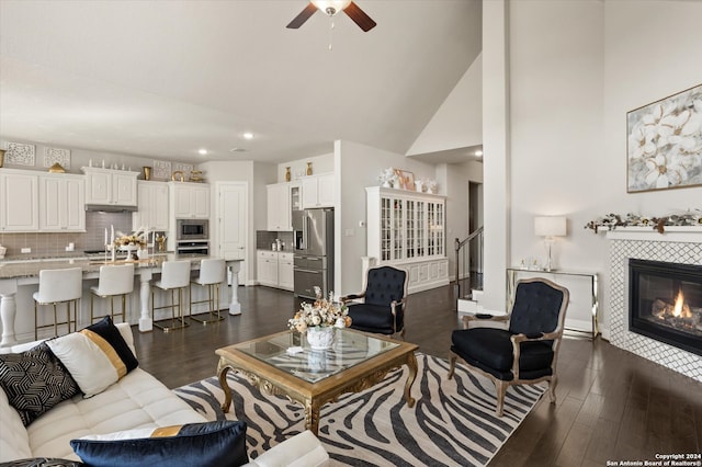 living room featuring ceiling fan, high vaulted ceiling, a tile fireplace, and dark hardwood / wood-style flooring