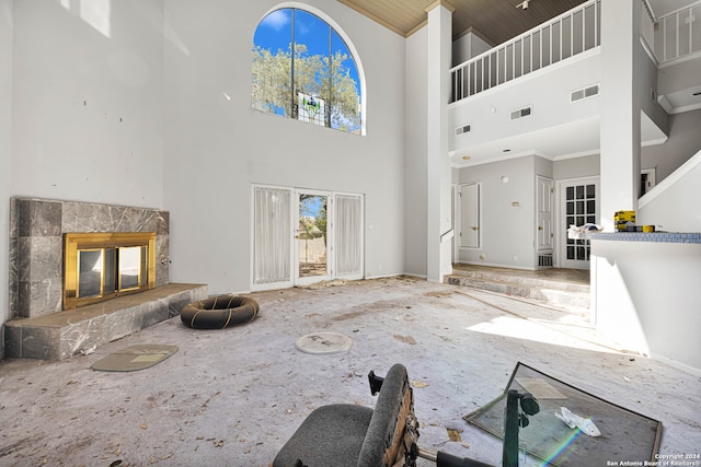 unfurnished living room with a high ceiling, crown molding, and a tiled fireplace