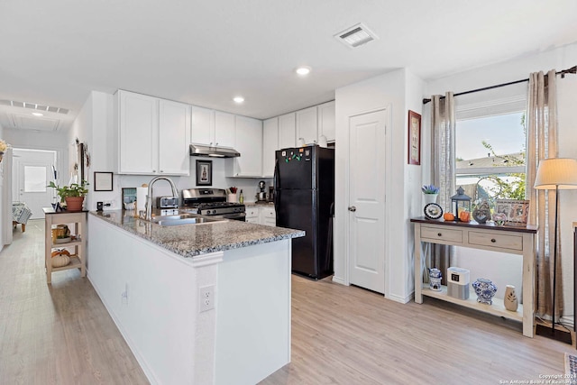 kitchen featuring black fridge, kitchen peninsula, stainless steel gas range, white cabinetry, and light hardwood / wood-style flooring