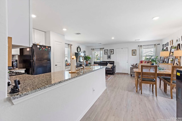 kitchen featuring light stone counters, black fridge, plenty of natural light, and white cabinetry