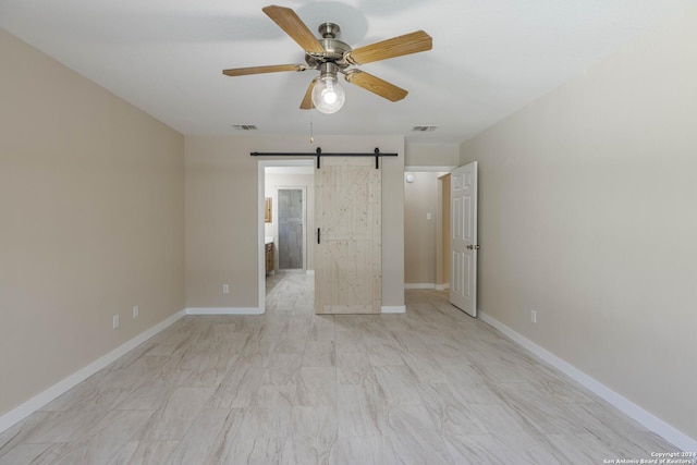 spare room featuring a barn door, visible vents, baseboards, and ceiling fan