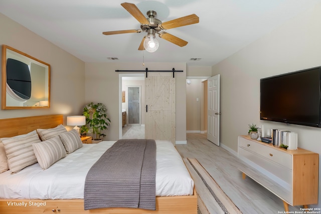 bedroom featuring light wood-type flooring, ensuite bath, ceiling fan, and a barn door