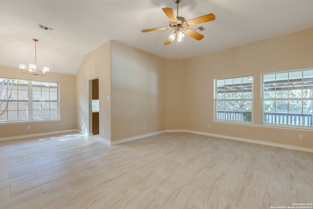 empty room featuring ceiling fan with notable chandelier, plenty of natural light, and vaulted ceiling