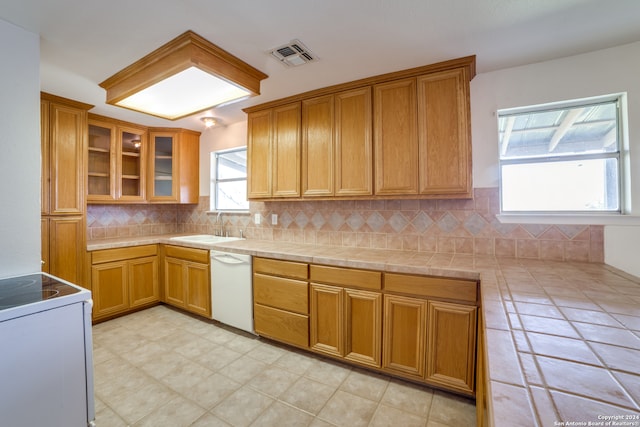 kitchen featuring white dishwasher, tile countertops, backsplash, and sink