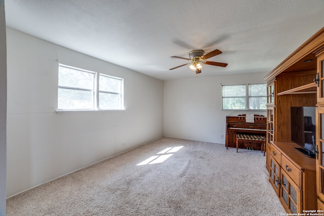 unfurnished living room featuring ceiling fan, light colored carpet, and a textured ceiling