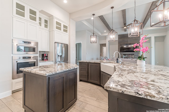 kitchen with sink, stainless steel appliances, white cabinetry, and decorative light fixtures