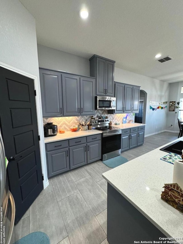 kitchen with gray cabinets, stainless steel appliances, backsplash, and a textured ceiling