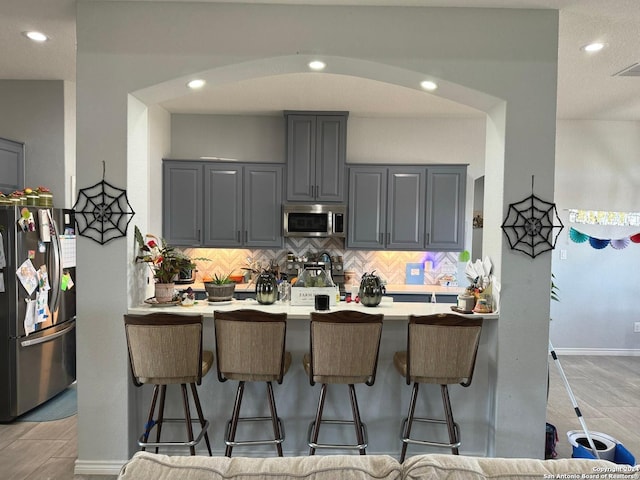 kitchen with light wood-type flooring, decorative backsplash, stainless steel appliances, gray cabinetry, and a kitchen breakfast bar