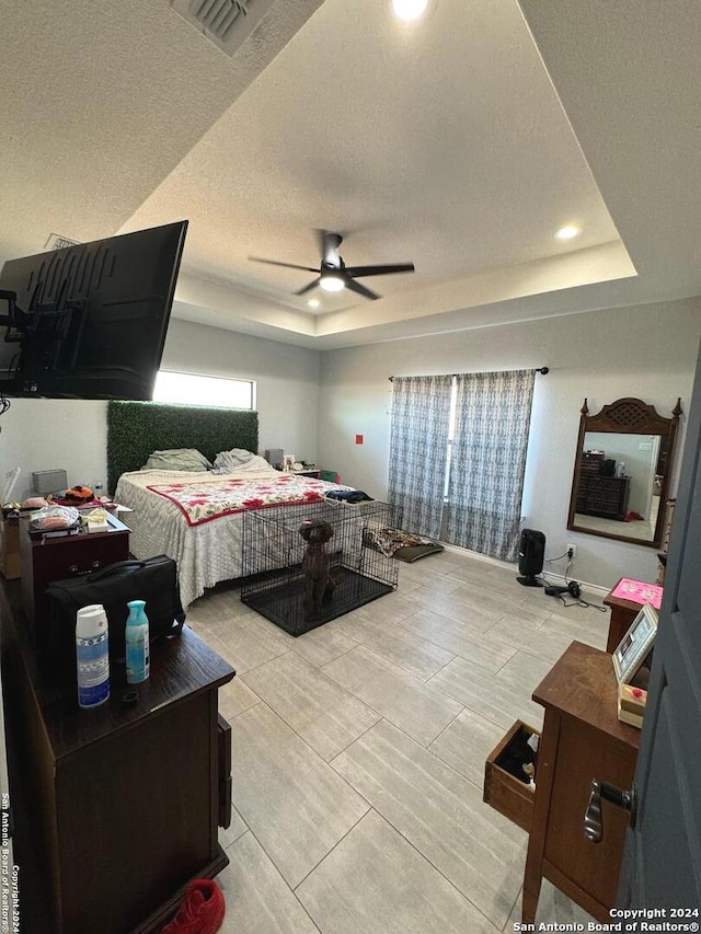 bedroom featuring ceiling fan, a textured ceiling, and a tray ceiling