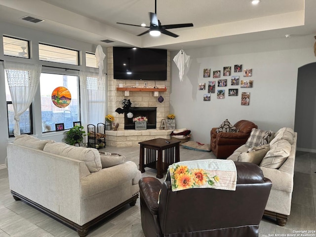 living room featuring ceiling fan, light hardwood / wood-style flooring, and a stone fireplace