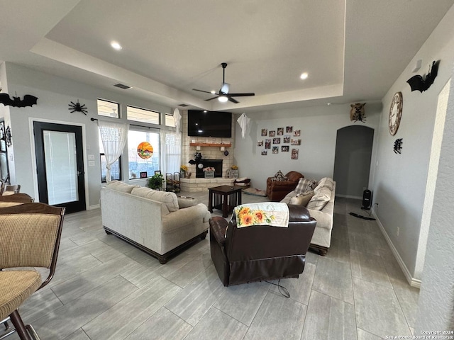 living room featuring a fireplace, ceiling fan, a tray ceiling, and light hardwood / wood-style flooring